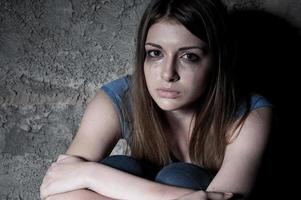 Hopelessness. Top view of young woman crying and looking at camera while sitting against dark wall photo