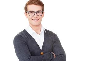 confiado y creativo. un joven alegre con los brazos cruzados y sonriendo a la cámara mientras está aislado en blanco foto