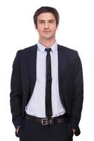 Relaxed businessman. Handsome young man in formalwear holding hands in pockets and looking at camera while standing isolated on white background photo