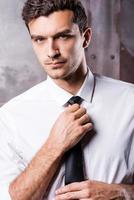 Elegant and handsome. Handsome young man in formalwear adjusting his necktie and looking at camera photo