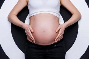 Pregnant belly. Cropped image of pregnant woman holding hands on belly while standing against target background photo