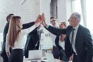 Cheerful business team giving each other high five to success while working in the modern office photo