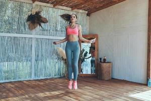 Full length of beautiful young woman in sports clothing using jumping rope on patio photo