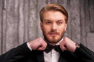 Tying a bow tie. Handsome young man in formalwear adjusting his bow tie and looking at camera photo