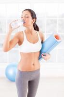 Staying refreshed. Attractive young woman in sports clothing drinking water while holding an exercise mat in sport club photo