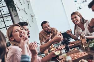 muy divertido juntos un grupo de jóvenes con ropa informal comiendo y sonriendo mientras cenan foto