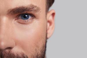 Looking deeply into your heart.  Close up of good looking young man half face looking at camera while standing against grey background photo