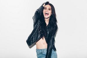 Carefree fun. Playful young woman in unbuttoned leather jacket having fun and expressing positive emotion while standing against grey background photo