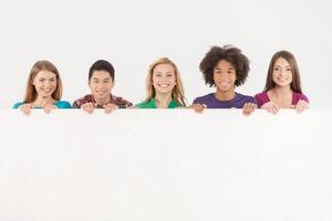 Friends with copy space. Cheerful young multi-ethnic people holding copy space and smiling at camera while isolated on white photo