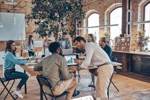 Group of young modern people in smart casual wear communicating and using modern technologies while working in the office photo