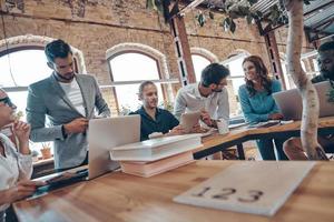 Group of young modern people in smart casual wear communicating and using modern technologies while working in the office photo