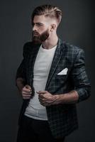 Confident look. Stylishly dressed young man looking away and adjusting his jacket while standing against grey background photo