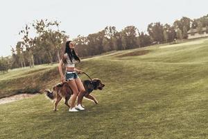 Dogs make life better. Full length of beautiful young woman playing with her dog and smiling while running outdoors photo