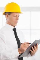 Foreman. Confident mature man in formalwear and hardhat writing something in his note pad photo