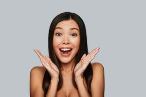 No way Surprised young Asian woman looking at camera and smiling while standing against grey background photo