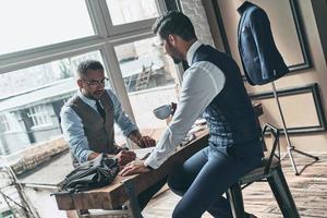 Achieving success as a designer. Young fashionable designer choosing fabric with his client while sitting in the workshop photo