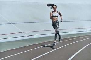 empujando fuerte toda la longitud de una mujer joven con ropa deportiva trotando mientras hace ejercicio al aire libre foto