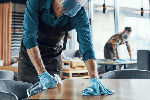 jóvenes camareros masculinos en mesas de limpieza de ropa de trabajo protectora en el restaurante foto