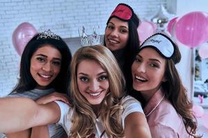 This one goes in frame. Self portrait of four playful young women smiling and looking at camera while having a slumber party photo