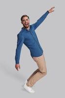 Going crazy. Full length of playful young man dancing and smiling while standing against grey background photo