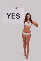 Better yes than no.  Full length of attractive young woman holding a poster and smiling while standing against grey background photo