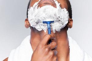 Close up of man shaving. Close up of young African man shaving his face while standing against grey background photo