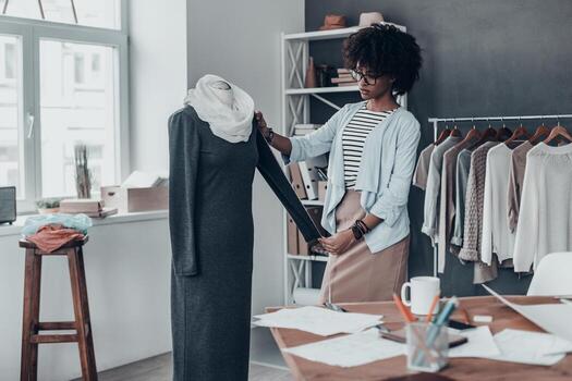 desarrollo de nueva línea de moda. joven africana concentrada midiendo manga con cinta mientras está de pie en su taller con ropa colgada en el fondo foto