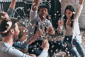 Unleashed fun. Top view of modern young people throwing confetti and smiling while drinking champagne indoors photo