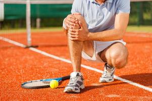 lesion deportiva. primer plano de tenista tocando su rodilla mientras está sentado en la cancha de tenis foto