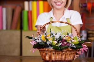 Making your life bright and colored. Cropped image of young blond hair woman in apron stretching out basket full of flowers and smiling photo