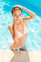 Beauty at the swimming pool. Top view of beautiful young woman in white bikini standing at the pool and looking at camera photo