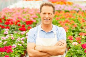 Flowers expert. Top view handsome mature man standing in flower bed and smiling photo