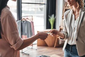 Buying and selling. Close up of young woman giving a credit card to salesperson while shopping in the fashion boutique photo