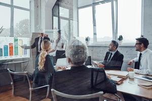 hombre de negocios moderno que realiza presentaciones y analiza datos en el gráfico mientras se reúne el personal en la sala de juntas foto