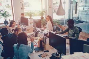 Group of young modern people in smart casual wear communicating and using modern technologies while working in the office photo