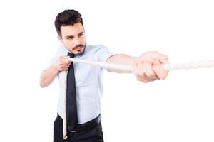 Everyday winner. Confident young man in shirt and tie pulling a rope while standing against white background photo