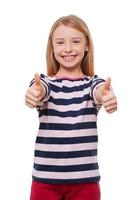 Happy little girl. Cheerful little girl showing her thumbs up while standing isolated on white photo