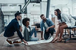 Lluvia de ideas para un nuevo proyecto. grupo de empresarios confiados en ropa informal inteligente que se comunican juntos y sonríen mientras trabajan en la oficina moderna foto