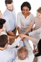 Working as one team. Top view of positive diverse group of people in smart casual wear keeping their hands clasped and smiling while standing close to each other photo