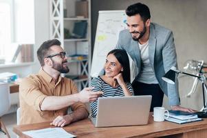 Finding solution together. Group of confident business people in smart casual wear discussing something while sitting at the desk in office photo