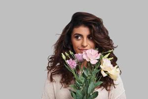 Flowers for her. Attractive young woman holding bunch of flowers and looking away while standing against grey background photo