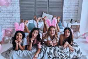 chicas perfectas. vista superior de cuatro mujeres jóvenes juguetonas con orejas de conejo haciendo una cara y sonriendo mientras están acostadas en la cama foto