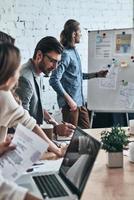 Sharing ideas. Modern young man pointing at flipchart while conducting a presentation in the board room photo