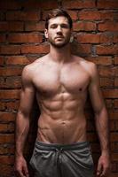 Strength and masculinity. Handsome young muscular man posing while standing against brick wall photo