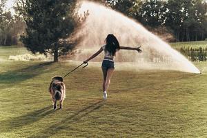 Full length rear view of beautiful young woman playing with her dog while running outdoors photo