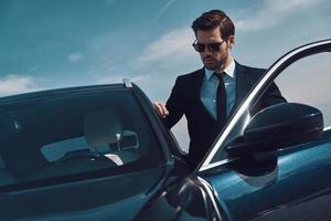 Time is money. Handsome young man entering his car while standing outdoors photo