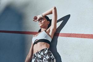 Killing workout. Top view of young woman in sports clothing keeping eyes closed while lying on the running track outdoors photo