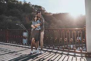 Full length of handsome man embracing young attractive woman while standing on the bridge outdoors photo