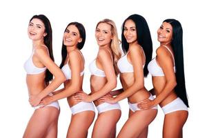 Loving their curves. Side view of five beautiful women in white lingerie looking at camera and smiling while bonding to each other and standing against white background photo