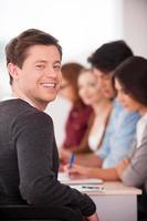 Confident in his team. Rear view of handsome young man looking over shoulder and smiling while sitting together at the table with another people photo